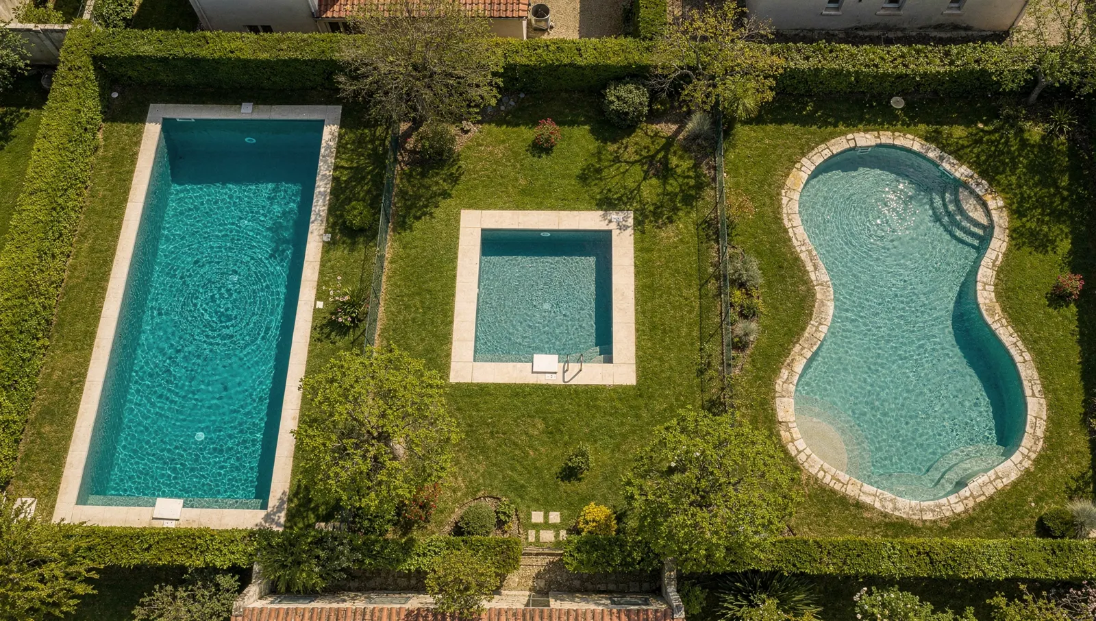 Vue aérienne de trois piscines de formes différentes dans des jardins voisins
